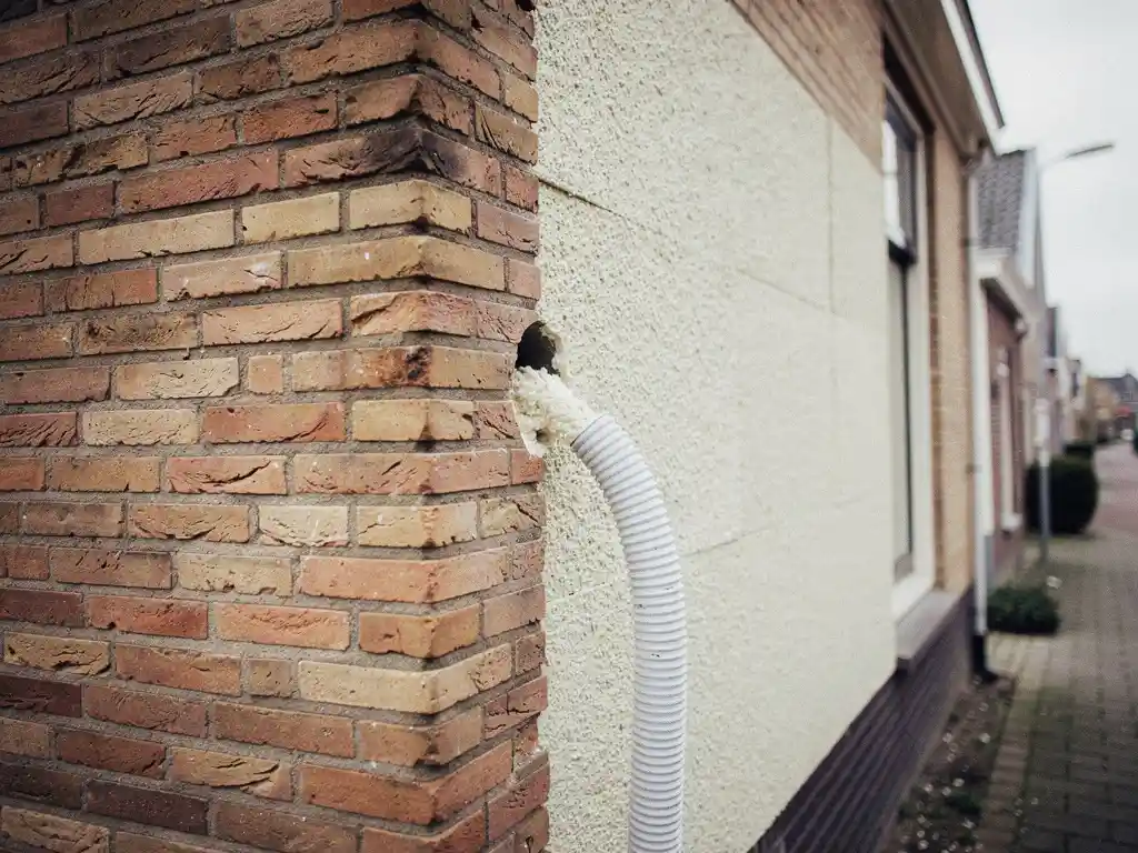 Spouwmuurisolatie in een Nederlandse hoekwoning met zichtbaar ingeblazen isolatiemateriaal bij een boorgat in de bakstenen gevel.
